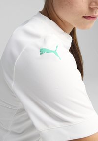 White sports shirt featuring a textured fabric, a round neckline, and a light teal Puma logo embroidered on the left shoulder.