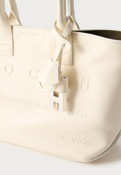 Τσάντα tote από κρεμ δέρμα με ανάγλυφη επωνυμία, διπλές λαβές και ασημένια μεταλλικά στοιχεία, με χαρακτηριστικό κούμπωμα και απαλή υφή.