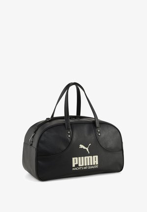 Geantă de voiaj neagră Puma cu două mânere și text bej cu sigla „PUMA MACHT'S MIT QUALITÄT” pe partea din față, vedere oblică pe fundal alb.