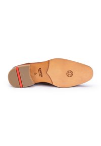 Semelle de chaussure en cuir fauve avec une forme pointue, talon en caoutchouc et accent rouge. Logo et texte estampillés sur la semelle intérieure, texture lisse et durable.