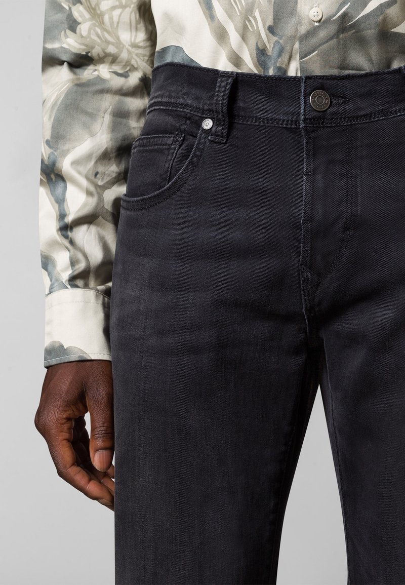 Pantalones vaqueros negros de denim con ajuste de tiro medio, que presentan un diseño estándar de cinco bolsillos y una textura sutil, combinados con una camisa estampada.