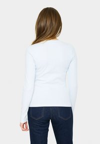 Ljusblå långärmad topp i ribbat tyg. Tätt sittande design med rundad halsringning, matchad med mörka denimbyxor.