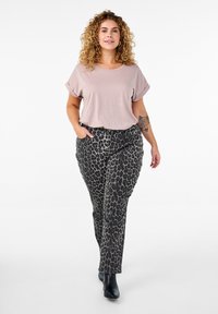 Jasnoróżowa bluzka z krótkim rękawem w połączeniu z czarno-szarymi spodniami w panterkę. Modelka nosi czarne botki za kostkę. Gładki materiał, luźny krój.
