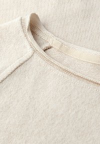 Beige, strukturiertes Gewebe im Nahaufnahme mit einem runden Ausschnitt. Es weist ein feines Rippmuster und glatte Nähte entlang der Kanten auf.