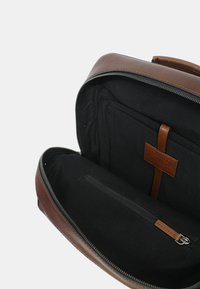 Borsa in pelle marrone con chiusura con zip. L'interno presenta una fodera in tessuto nero, una tasca con zip e un compartimento piatto fissato con una cinghia in pelle.