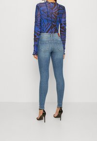 Long-sleeve blue and black zebra-patterned top paired with fitted light blue jeans and black high-heeled shoes, viewed from the back.