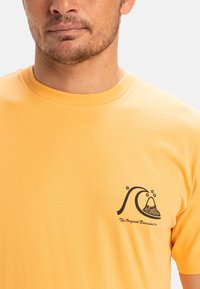 Short-sleeve, round-neck t-shirt in vibrant yellow cotton. Features a black logo design of waves and a mountain on the left chest.