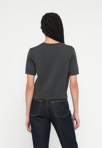 Pulover gri, tricotat, cu mâneci scurte și decolteu rotund. Lungime scurtă, cu tiv ondulat. Purtat cu blugi de culoare albastru închis.