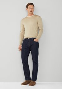 Beżowy sweter robiony na drutach, ciemnoniebieskie dżinsy i brązowe zamszowe buty. Sweter ma okrągły dekolt; dżinsy mają kieszenie z przodu i prosty krój.