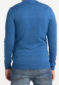 Maglione blu a maglia con maniche lunghe e polsini a costine. Tessuto liscio, design aderente e schiena semplice con dettagli minimi. Indossato sopra jeans di denim.