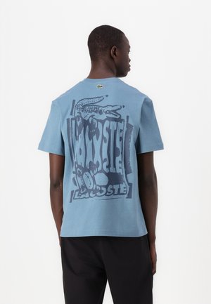 Kortärmad blå bomulls-T-shirt med en stor grafisk bild av en krokodil och text på baksidan. Rundhalsdesign med avslappnad passform.