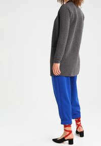 Szara pikowana kurtka z długimi rękawami, zestawiona z niebieskimi luźnymi spodniami. Dopełnieniem stroju są czerwone buty na sznurowadła na obcasie. Widoczne są szczegóły faktury materiału.