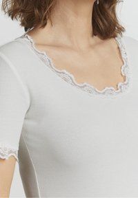 Bílý žebrovaný top s krátkým rukávem a krajkovým výstřihem se scalloped lemem. Slim fit a hladká textura, detaily na rukávech a límci.