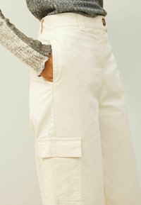 Crème-kleurige cargo broek met een comfortabele pasvorm, voorzien van een zijzak en een soepel, lichtgewicht stof. De tailleband heeft een knoopsluiting.