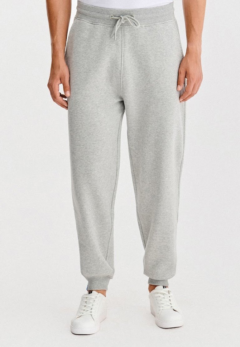 Szare spodnie dresowe z elastycznym pasem i sznurkiem, zwężanymi nogawkami oraz ściągaczami na dole. W połączeniu z białymi trampkami.