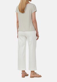 Jasnoszara bluzka z krótkim rękawem, uszyta z miękkiej tkaniny, w połączeniu z białymi spodniami o szerokich nogawkach oraz brązowymi sandałami z srebrnymi akcentami.