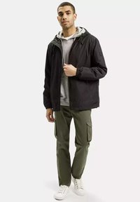 Czarna kurtka z kapturem, szary sweter pod spodem, oliwkowe spodnie cargo i białe trampki. Prosty design z elastycznymi mankietami i kieszeniami.