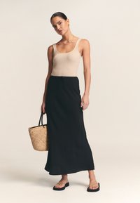 Beiger, gerippter Tanktop, schwarzer Maxirock mit Kordelzug in der Taille, braune gewebte Handtasche und schwarze Flip-Flops. Glatte Texturen und schlichtes Design.