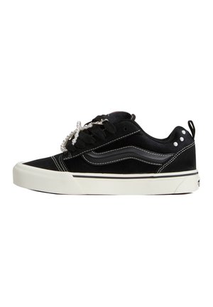 Sort lavtop sneakers med hvid sål, hvid syning og dekorative perlesnørebånd på hvid baggrund, sidevisning.