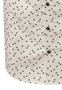 Camicia beige con un piccolo motivo floreale nero, con bottoni neri e una texture liscia. I dettagli includono accenti floreali distribuiti in modo uniforme.