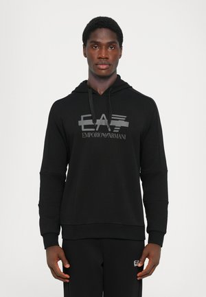 Črna kapuca z logotipom spredaj, ki prikazuje "EA" in "EMPORIO ARMANI." Narejena iz mehkega materiala, z sproščenim krojem in vrvico na kapuci.