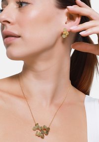 Set di gioielli dorati composto da orecchini a bottone e una collana con pendenti circolari e testurizzati, mostrati sul collo e sull'orecchio di un modello.