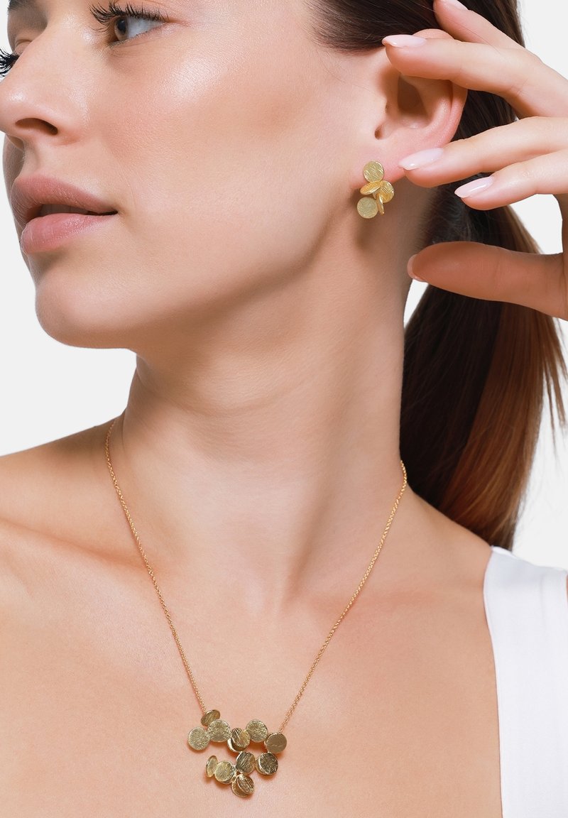 Set di gioielli dorati composto da orecchini a bottone e una collana con pendenti circolari e testurizzati, mostrati sul collo e sull'orecchio di un modello.