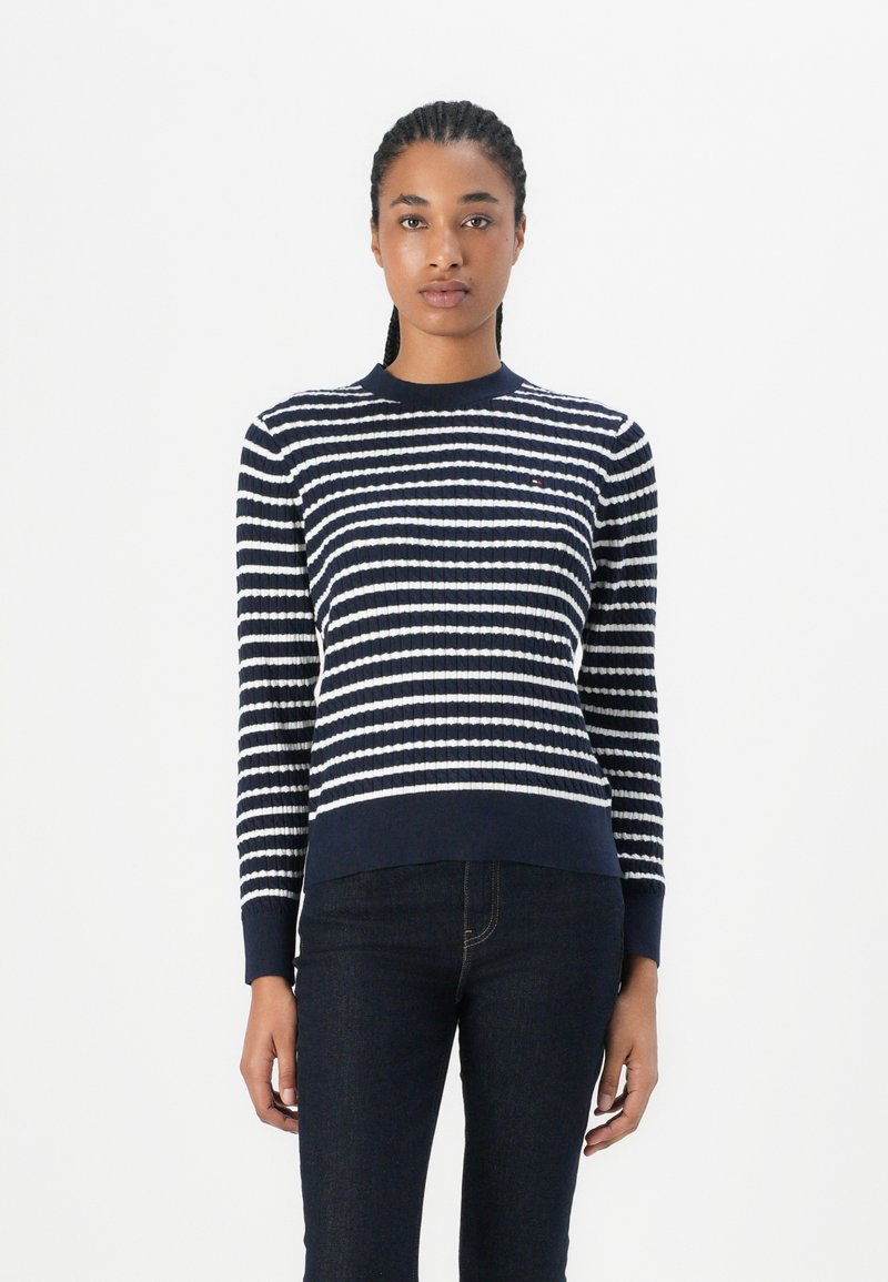 Navy en witte gestreepte gebreide sweater met een ribbelstructuur, ronde hals en lange mouwen; gecombineerd met donkere spijkerbroeken.
