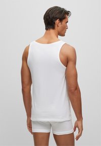 Un débardeur en coton blanc avec un col rond et de larges bretelles, associé à un short boxer blanc, vu de dos.