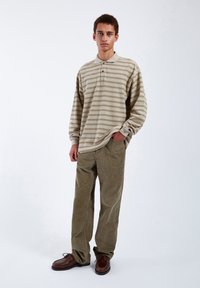 Beige pruhované polo s dlouhým rukávem a límečkem, doplněné olivovými manšestrovými kalhotami a hnědou obuví. Jednoduchý design, uvolněný střih.