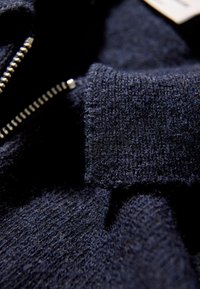 Granatowy dzianinowy materiał o gładkiej fakturze, z zamkiem błyskawicznym i prążkowanym kołnierzykiem. Zbliżenie podkreśla szczegóły materiału.