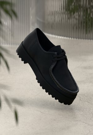 Sorte lærersko med en tykk, teksturert såle og dekorativ søm. Har rund tå og snøring. Lett og minimalistisk stil.