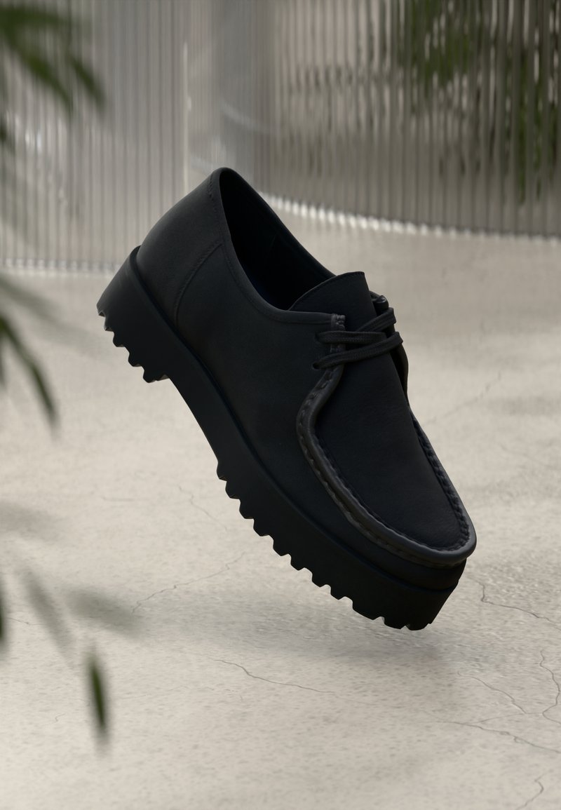 Shoe de couro preto com uma sola grossa e texturizada e costura decorativa. Apresenta bico redondo e design com atacadores. Estilo leve e minimalista.