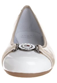 Scarpa piatta beige con punta lucida bianca, tomaia in tessuto testurizzato e un accento logo argentato rotondo nella parte anteriore. Fodera interna morbida.