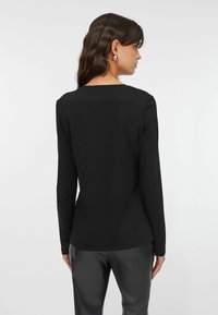 Top nero a maniche lunghe con scollo tondo, realizzato in tessuto liscio. Presenta una silhouette aderente e un design semplice, senza motivi o elementi decorativi visibili.