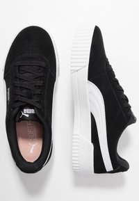 Černé semišové tenisky s bílou podešví, šněrovací design a detail loga na boku. Měkká stélka pro pohodlí, texturované bílé akcenty na podešvi.
