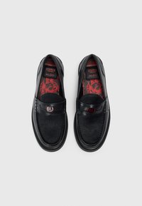 Sorte slip-on sko med et glatt skinn-overdel og pelsaktig tekstur. Innredningen har en rød mønstrete såle med merkevare detaljer.