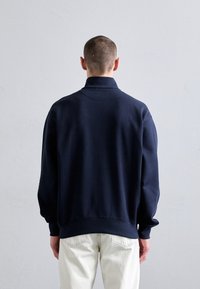 Maglione pullover blu navy con colletto alto, realizzato in tessuto morbido, con polsini e orlo a coste, e vestibilità rilassata.