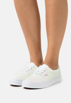 Baskets blanches avec une tige pailletée et vert clair, ornées d'œillets en métal et de lacets blancs. Semelle en caoutchouc avec un logo sur le côté.