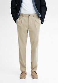 Pantaloni beige a pieghe con taglio diritto, la trama del tessuto appare liscia e presenta passanti per cintura, tasche anteriori e chiusura a bottone.