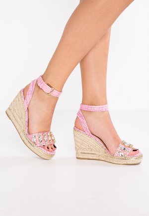 Sandały na koturnie z różowymi tekstylnymi paskami ozdobionymi przezroczystymi kamieniami oraz plecioną podeszwą espadrylową. Model posiada pasek na kostkę z klamrą.