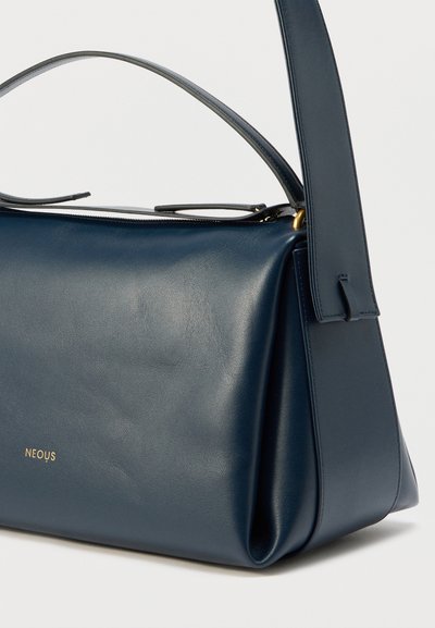 Navyblå læderhåndtaske med et struktureret design, glat tekstur og gyldent logo. Har et enkelt håndtag og lynlås.