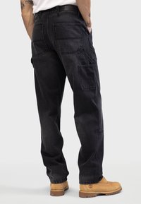 Mørkegrå cargo bukser lavet af denim, med flere lommer, afslappet pasform og lige ben design. Båret med brune arbejdssko.