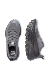 Grå sportskor med nät- och syntetmaterial, texturerad ovandel, robust sula i svart gummi med framträdande greppklackar. Minimal varumärkesprofil.