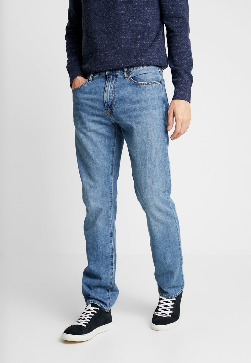 Ljust blå denim jeans med rak skärning och subtila slitningar. Bärs med en mörkblå texturerad tröja och svarta sneakers.
