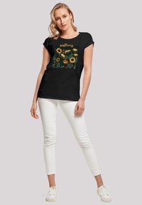Black cotton t-shirt with short sleeves, featuring a sunflower graphic in yellow and green on the front. Paired with white skinny jeans and white sneakers.