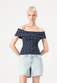 Marinbluse med avtagne skuldre, små blomster mønstre, ribbet tekstur, tettsittende design, kombinert med lyseblå distressed denimshorts.