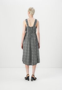 Μαύρο και άσπρο φλοράλ μίντι φόρεμα με σμιχτό πίσω μέρος, φαρδιές τιράντες και φουσκωτό φούστα, συνδυασμένο με μαύρες γόβες με τακούνι.