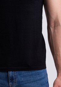 Černý bezrukávový top vyrobený z hladkého, lehkého materiálu, spárovaný s modrými džíny z denimového materiálu s klasickým designem pěti kapes.