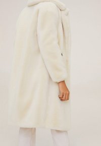 Wit nepbontjas met een brede kraag, lange mouwen en een losse pasvorm. De textuur lijkt zacht met een egale oppervlakte en geen zichtbare patronen.